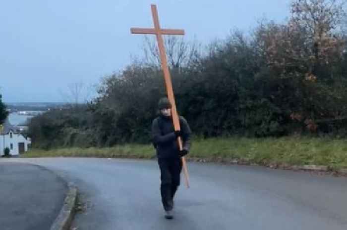 A man is walking across Wales with a huge cross on his back