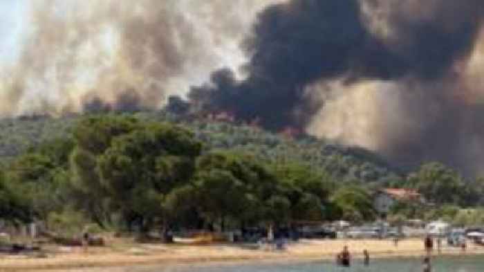 Beachgoers look on as wildfires burn in Greece