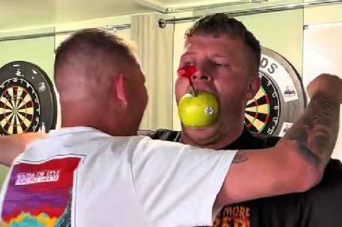 Darts pro Nathan Aspinall throws dart at influencer with apple in his mouth